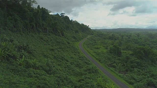 航拍图:令人惊叹的郁郁葱葱的绿色自然在空旷的道路附近的山坡上蔓生。视频素材