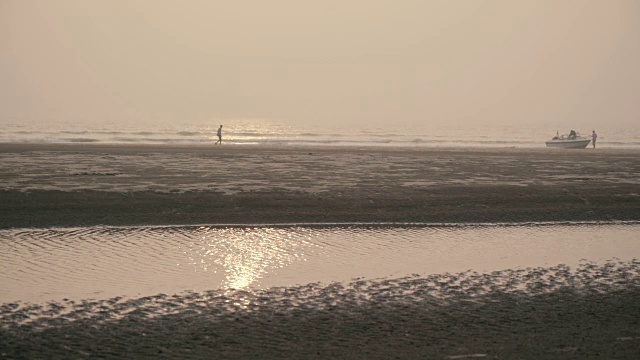 夕阳在海滩上，人们在远处上了船视频素材