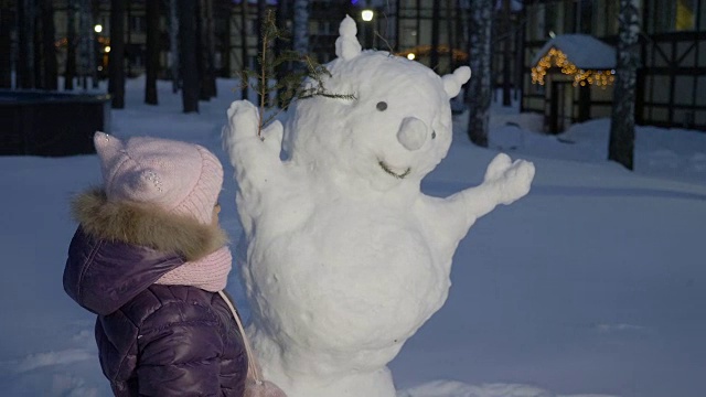 小女孩在雪地里堆雪人，看着它视频素材