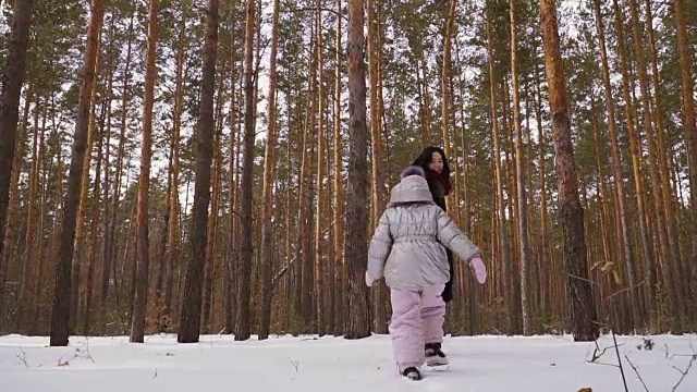 一个年轻的女人带着小女儿在冬天的森林里散步视频素材