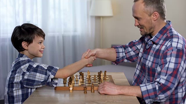 男孩跟爸爸下棋赢了，小孩跟爸爸握手，爱好视频素材