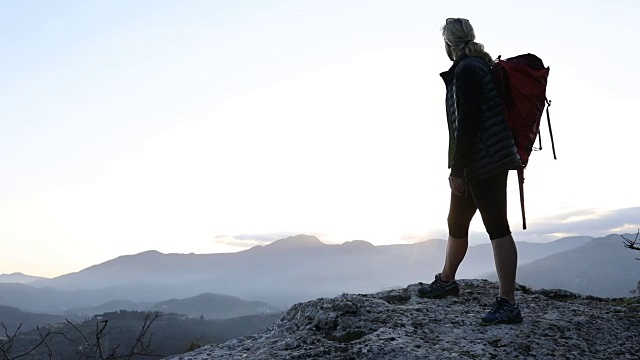 日出时，一名女性徒步旅行者在山谷上空停留视频素材