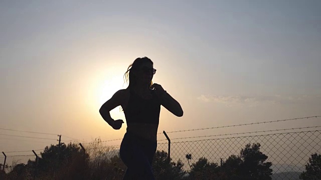 日出时，跟随运动女孩在乡间小路慢跑。年轻女子在户外晨跑。健康积极的生活方式。慢镜头视频素材