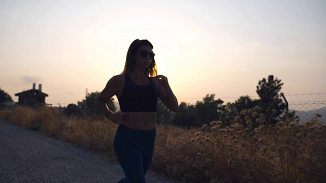 戴眼镜的运动女孩在日出时在乡村公路上慢跑。年轻女子在户外奔跑。健康积极的生活方式。慢镜头视频素材