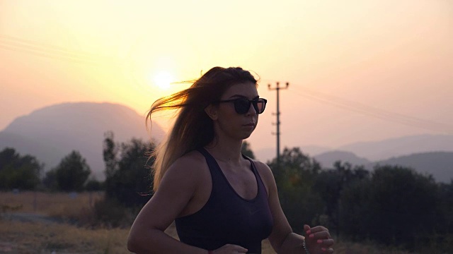 戴眼镜的运动女孩在日出时在乡村公路上慢跑。年轻女子在户外奔跑。健康积极的生活方式。慢镜头视频素材