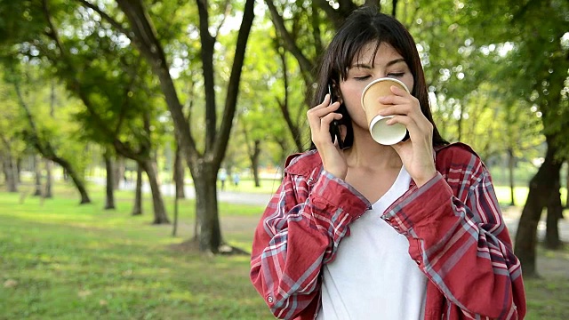 美女在公园里喝着咖啡，用智能手机聊天。视频素材