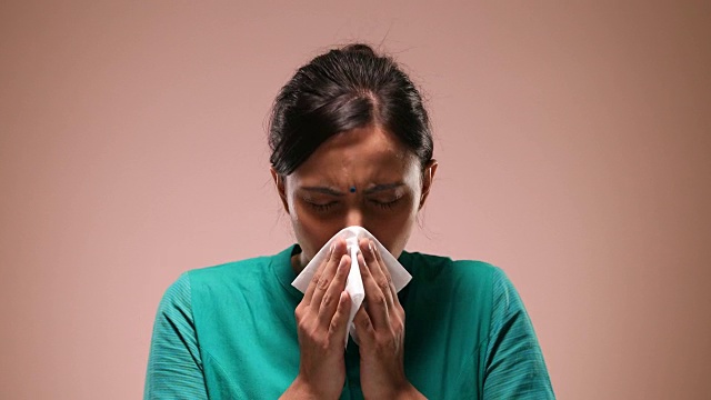 一名年轻女子站在粉红色背景下打喷嚏/印度新德里视频素材