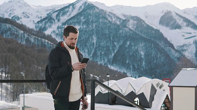 男人用手机发送信息，站在户外的滑雪基地在山上视频素材