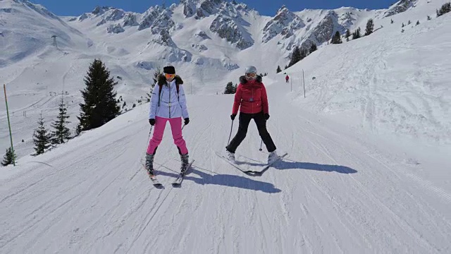 两名女子滑雪者在冬季沿着理想的山坡滑雪视频素材