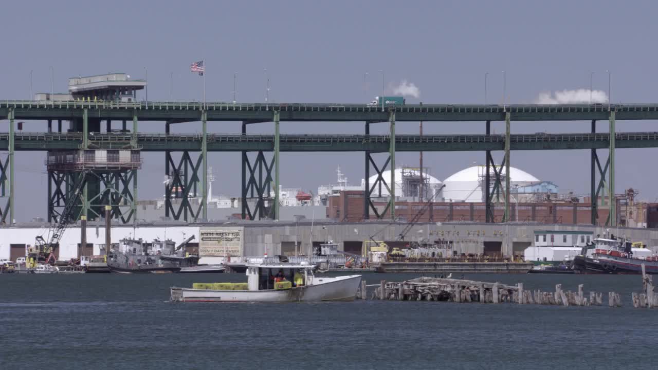 广角渔船或船在海湾，港口，码头，或河流附近的桥梁，背景砖建筑或仓库。可能是捕鱼区或工业区。海鸥或鸟类在水上飞行。莫里斯j.托宾纪念桥(神秘河桥视频素材