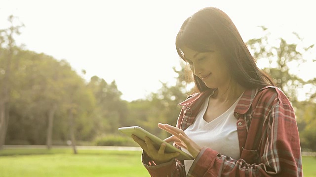 年轻美丽的女人使用数字平板电脑在阳光早上在公园，有吸引力的女人触摸屏数字平板电脑搜索信息视频素材