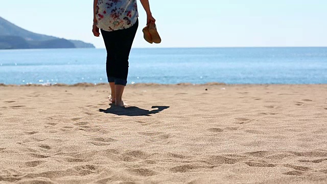 赤脚的女人走在沙滩上走向大海视频素材