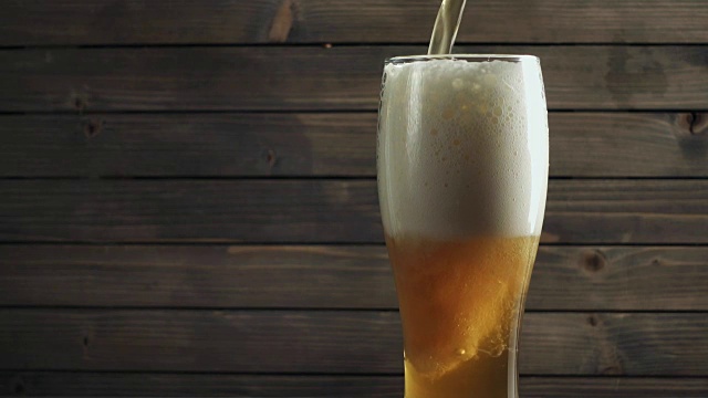 啤酒倒在玻璃上的木材背景。慢动作视频素材