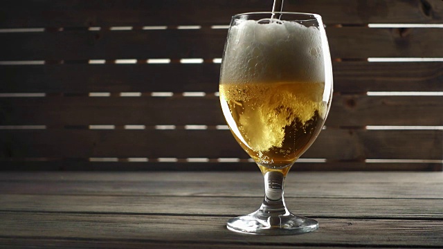 啤酒倒在玻璃上的木材背景。慢动作视频素材