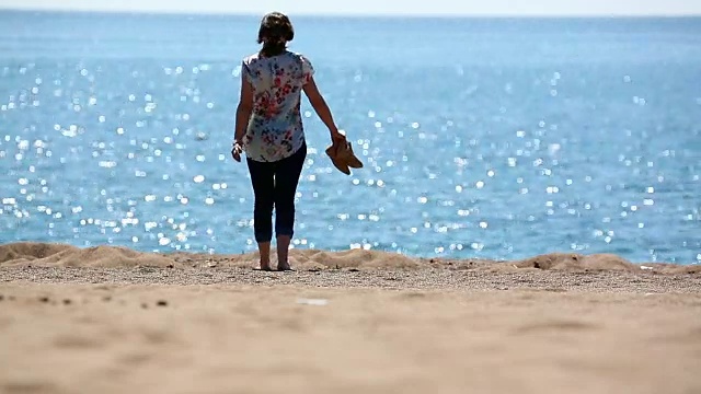 赤脚的女人走在沙滩上走向大海视频素材