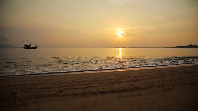 沙滩上的沙子和海浪伴着小船和夕阳视频素材