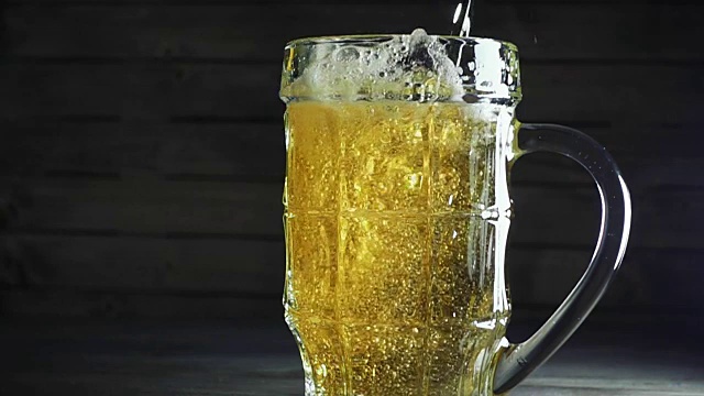 往啤酒杯里倒啤酒的慢镜头。在深色的木质背景上视频素材