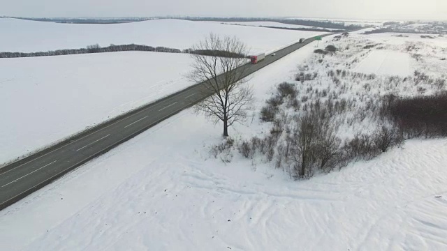 空中拍摄的卡车和汽车行驶在雪地里的冬季道路上。视频素材