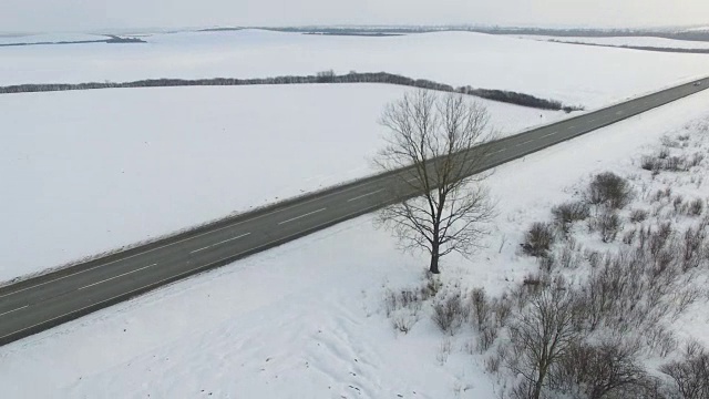 空中拍摄的卡车和汽车行驶在雪地里的冬季道路上。视频素材