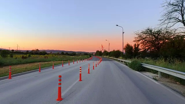 在日出、日落时驾驶穿过标有交通锥的单车道道路工作区域视频素材