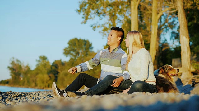 一对年轻夫妇在湖上休息，他们旁边是一只狗视频素材