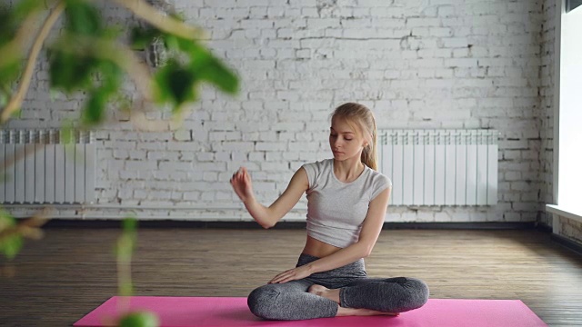 迷人的女孩正在练习瑜伽，弯曲到一边，手臂向上，然后放松在轻松的荷花姿势在健康中心的个别会议。灵活宁静冥想理念。视频素材