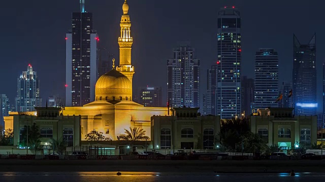 现代迪拜城市的天际线与拉希德Al Hadeeth清真寺在夜晚与水面上发光的摩天大楼的时间推移视频素材