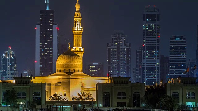 现代迪拜城市的天际线与拉希德Al Hadeeth清真寺在夜晚与水面上发光的摩天大楼的时间推移视频素材