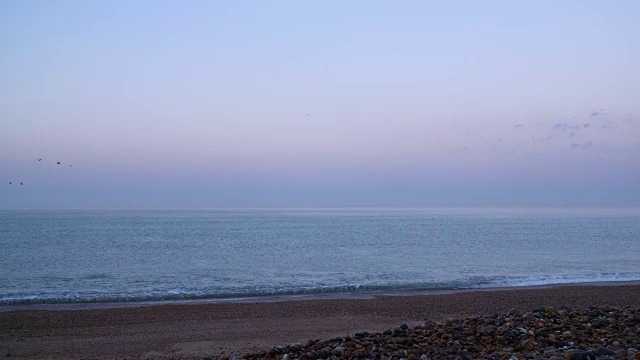 拂晓时海浪缓缓地滚上布莱顿海滩的长镜头。视频素材