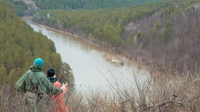 一对年轻的徒步旅行者站在河对岸的山顶上聊天视频素材