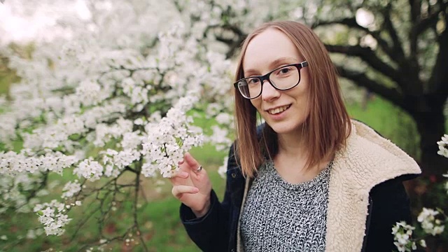 美丽快乐的年轻女子享受花香在春天的花园视频素材