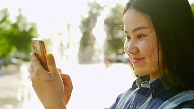 年轻漂亮的亚洲女人在喷水喷泉前使用手机视频素材