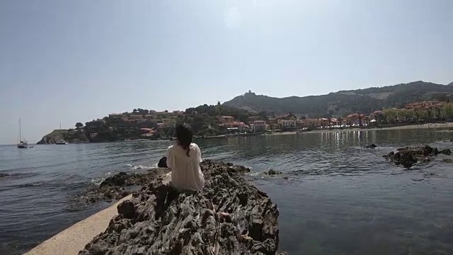 一名穿着裙子的年轻女子坐在法国科利乌尔的地中海边视频素材