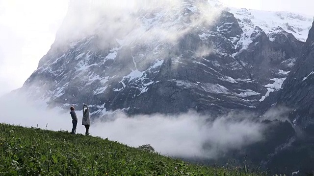 一对夫妇穿过高耸的雪峰下的草地视频素材