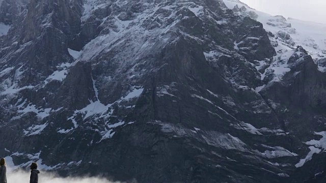 一对夫妇穿过高耸的雪峰下的草地视频素材