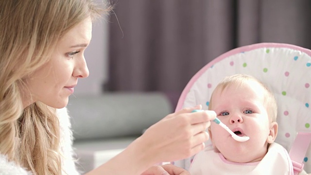 妈妈用勺子喂婴儿。小孩在婴儿椅上哭视频素材