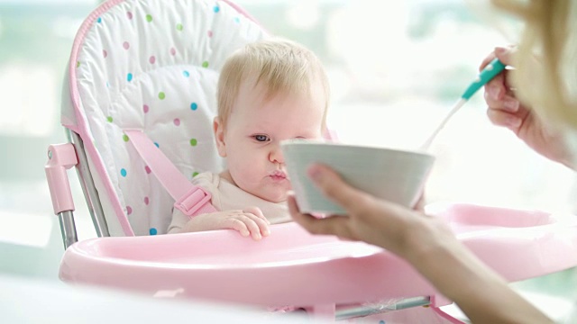 母亲给孩子喂婴儿食品。蹒跚学步的小女孩吃泥状食物视频素材