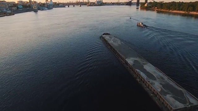 日落航拍画面显示，驳船在城市港口附近的河上航行视频素材