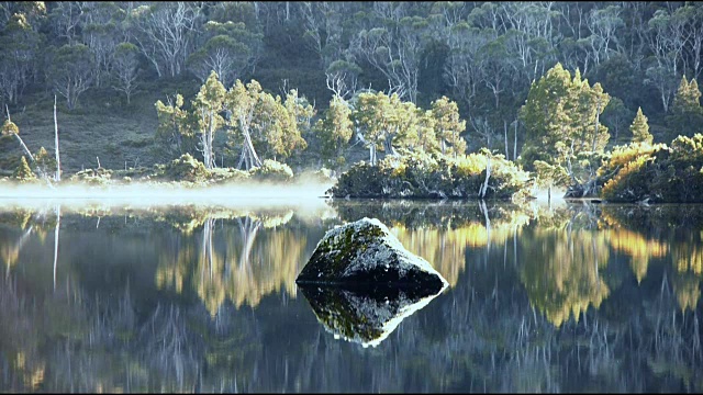 晨雾笼罩在平静的湖面上，湖面上有岩石视频素材