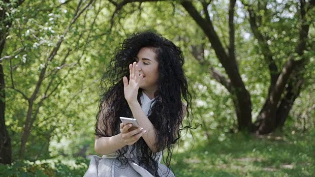 当她在花园里用手机的时候，一个漂亮的褐发女人和一个人打招呼视频素材