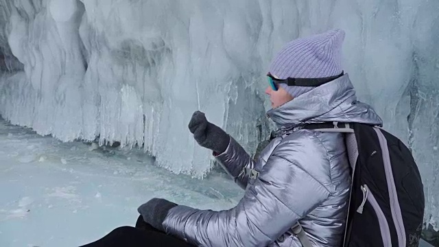 女人在贝加尔湖冰面上的旅行。冬岛之旅。女孩在冰岩石下行走。游客看着美丽的冰洞。极限跋涉和步行。背包客在大自然中休憩。视频素材