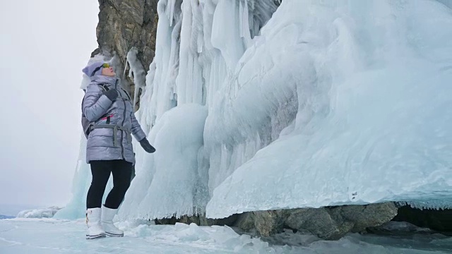 女人在贝加尔湖冰面上的旅行。冬岛之旅。女孩在冰岩石下行走。游客看着美丽的冰洞。极限跋涉和步行。背包客在大自然中休憩。视频素材