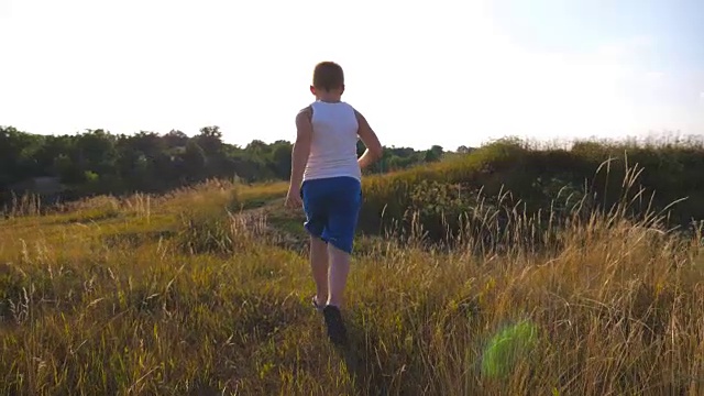 孩子们在户外草坪上慢跑。在阳光明媚的一天，一个小男孩在草地上跑步。男孩在夏天的草地上享受大自然的乐趣。慢镜头后景特写视频素材