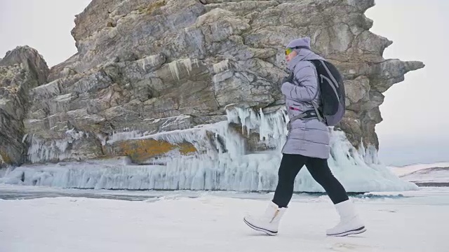 女人在贝加尔湖冰面上的旅行。冬岛之旅。女孩在冰岩石下行走。游客看着美丽的冰洞。极限跋涉和步行。背包客在大自然中休憩。视频素材