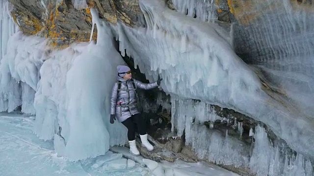 女人在贝加尔湖冰面上的旅行。冬岛之旅。女孩在冰岩石下行走。游客看着美丽的冰洞。极限跋涉和步行。背包客在大自然中休憩。视频素材