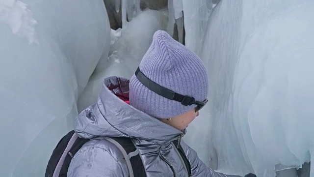 女人在贝加尔湖冰面上的旅行。冬岛之旅。女孩在冰岩石下行走。游客看着美丽的冰洞。极限跋涉和步行。背包客在大自然中休憩。视频素材