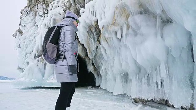 女人在贝加尔湖冰面上的旅行。冬岛之旅。女孩在冰岩石下行走。游客看着美丽的冰洞。极限跋涉和步行。背包客在大自然中休憩。视频素材