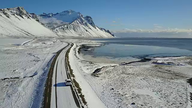 在冰岛东海岸的冬季，飞过冰雪覆盖的道路和雪山景观视频购买