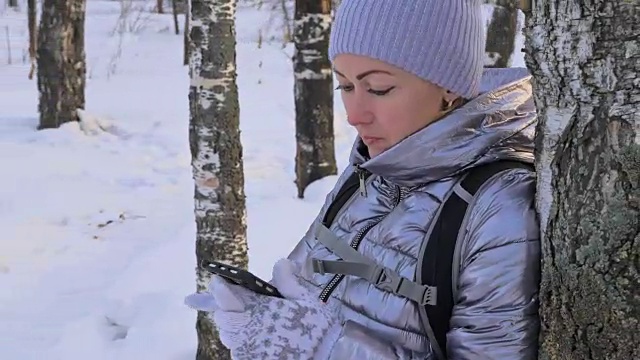 一个女人走在树林里。旅行者在森林里用手机拍照。女孩会自拍，用智能手机交流。美丽多汁的日落时分。视频素材