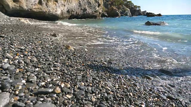 女性的脚在阳光灿烂的日子赤脚走海岸后视图。温柔的海浪拍打着年轻女子的脚走在卵石海滩上。暑假或假期的概念。视频素材